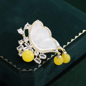 Close-up of a vintage butterfly brooch with white shell wings and tassels on green velvet