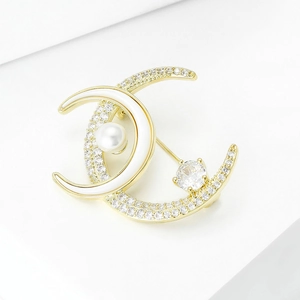 Elegant gold double crescent brooch with sparkling zircons and a white pearl on white background
