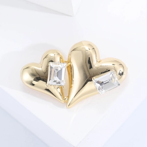 Détail d'une broche double cœur dorée avec cristaux rectangulaires sur socle blanc