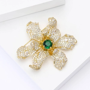 Elegant gold flower brooch with emerald stone and pavé zircons on white surface