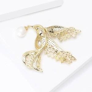 Elegant gold bird brooch with white pearl and sparkling zircons on white pedestal
