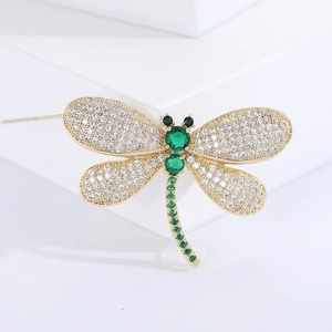 Detailed view of dragonfly brooch with gold plating, white zircons, and green gems