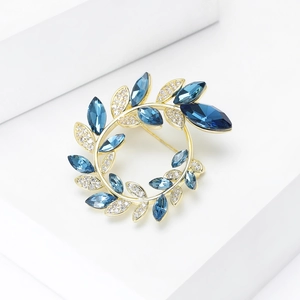 Gros plan d'une broche couronne de feuilles dorées avec cristaux bleus et zircons brillants