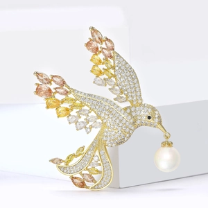 Elegant bird brooch in gold with zircon wings and a white pearl drop on white blocks