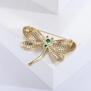 Elegant gold dragonfly brooch with crystal wings and green gemstones on white display