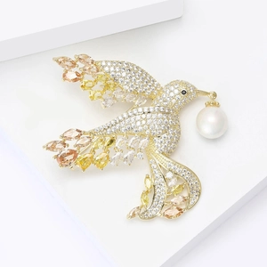 Exquisite golden bird brooch with colorful zircons and a white pearl on a white pedestal