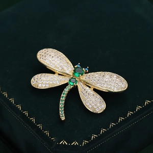 Elegant gold dragonfly brooch with white crystals and green gemstones on velvet