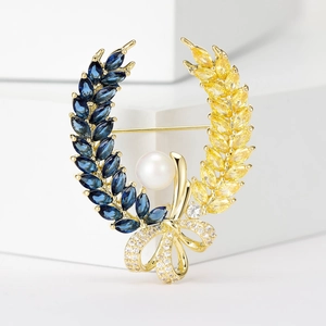 Macro shot of wheat wreath brooch with blue and yellow gems, pearl, and gold bow