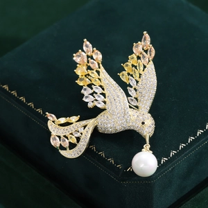 Close-up of golden bird brooch with colorful zircons and a white pearl on green velvet