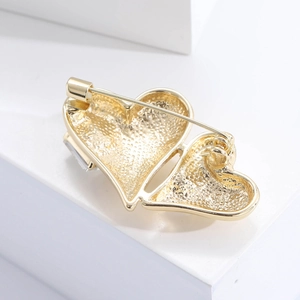 Détail macro d'une broche double cœur doré avec texture sablée et pierre en zircon cubique