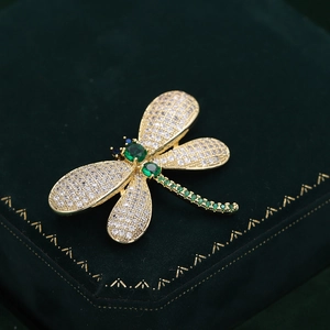 Macro detail of golden dragonfly brooch with zircon wings on green velvet jewelry box