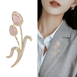 Elegant gold tulip brooch with pink gems and white zircons shown on grey blazer