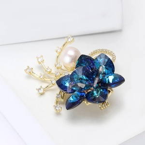 Squisita spilla a fiore con cristalli blu profondo, perla centrale e accenti in oro