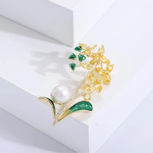 Détail d'une broche orchidée en émail vert avec cristaux jaunes et une grande perle blanche