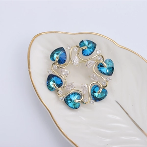 Eleganter Gold-Blumen-Brosche mit blauen Herzkristallen und Zirkonia auf weißem Tablett