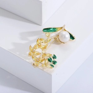 Détail d'une broche fleurie avec cristaux jaunes, émail vert et perle blanche