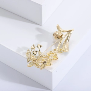 Détail d'une broche orchidée dorée avec zircons jaunes et perle sur fond épuré