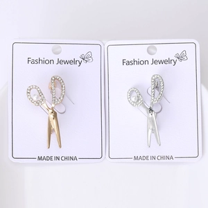 Detailed view of silver and gold scissor brooches with rhinestones and pearls on a card
