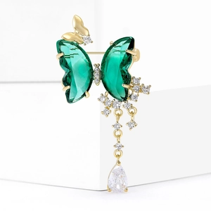 Exquisite gold butterfly brooch with green crystals and sparkling tassel drop on white podium