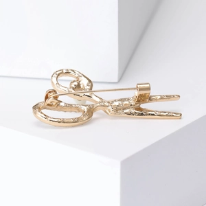Golden scissors brooch pin with engraved patterns on white geometric block display