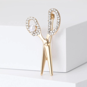 Elegant gold scissor brooch with crystal rhinestones and white pearl on a white pedestal