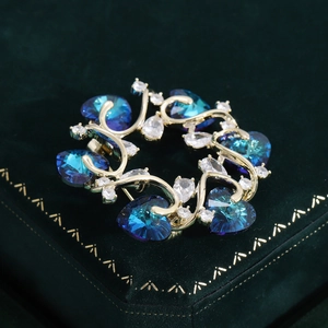 Eleganter goldener Kranz-Brosche mit blauen Herzkristallen und Zirkonia-Steinen