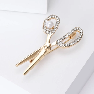 Macro detail of golden scissor brooch with sparkling rhinestones and a large white pearl