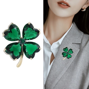 Élégante broche trèfle dorée avec cristaux de cœur verts sur fond blanc minimaliste