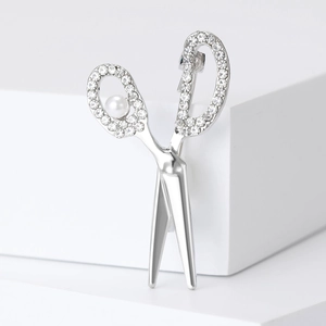 Macro detail of silver scissor brooch with sparkling rhinestones and white faux pearl