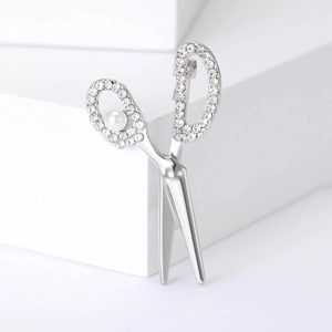 Close-up of silver scissors brooch featuring sparkling rhinestones and a white pearl accent