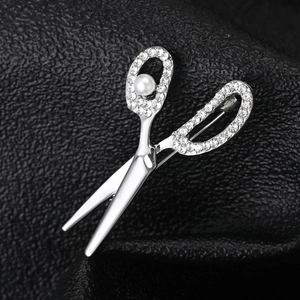Macro detail of scissor brooch with crystal rhinestones and pearl on black leather