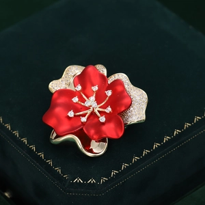 Dettaglio della spilla a fiore rossa e oro con zirconi bianchi su velluto verde