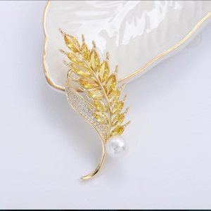 Close-up of golden wheat brooch with yellow stones and a pearl on white ceramic tray