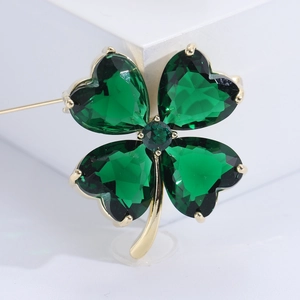Détail macro d'une broche trèfle doré avec des cristaux vert émeraude en forme de cœur