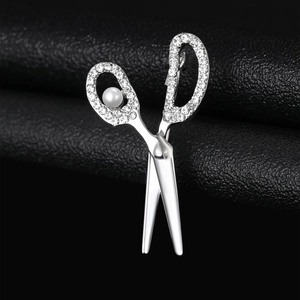 Detailed close-up of a silver scissor brooch with rhinestones and pearl on black leather