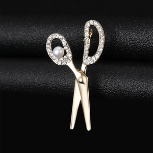 Macro detail of golden scissors brooch with rhinestones and pearl on black leather