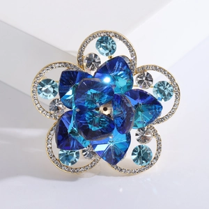 Broche fleur dorée élégante avec cristaux bleus et strass blancs sur support blanc pur