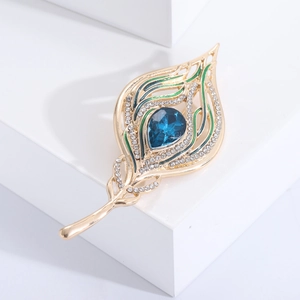Detailed macro shot of a peacock feather brooch with blue gems and green enamel on a white stand