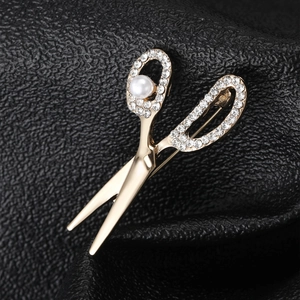 Detail of gold scissor brooch with crystal rhinestones and white pearl on black leather