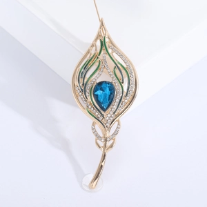 Elegant gold peacock feather brooch with blue crystal and green enamel on a white base