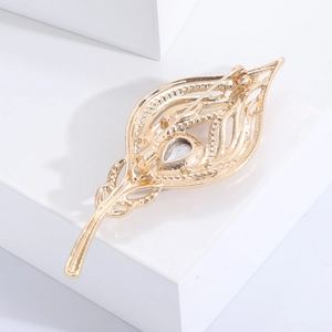 Elegant gold feather brooch with crystal teardrop stone on white geometric background