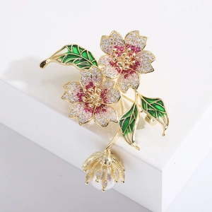 Detail of floral brooch with red zircon petals, green leaves, and a pearl drop