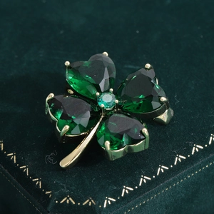 Vue macro d'une broche trèfle avec cristaux verts en cœur et tiges plaquées or