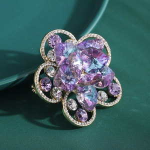 Makroaufnahme einer lila Kristallblumenbrosche mit Goldblüten und weißen Diamanten
