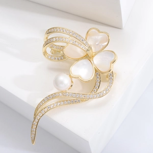Elegant gold clover brooch with white shell petals and a pearl center on a white stand