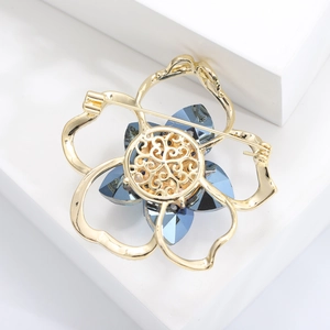 Detail of camellia brooch with blue crystals and gold metal frame on a white display