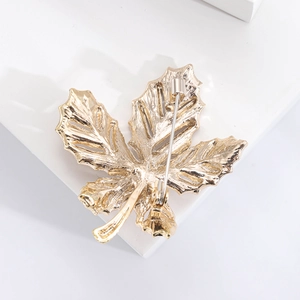 Detail view of gold maple leaf brooch back showing secure safety pin and metallic texture