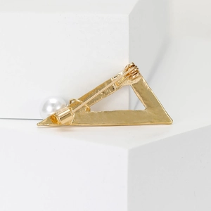Golden alloy triangle brooch with a large white pearl on white architectural cubes