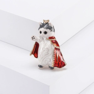 Broche de gato esmaltado con corona dorada y capa roja sobre un pedestal blanco