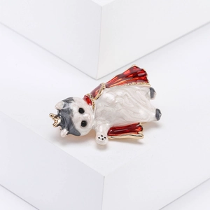 Detalle de broche de gato esmaltado con capa roja y corona dorada sobre soportes blancos